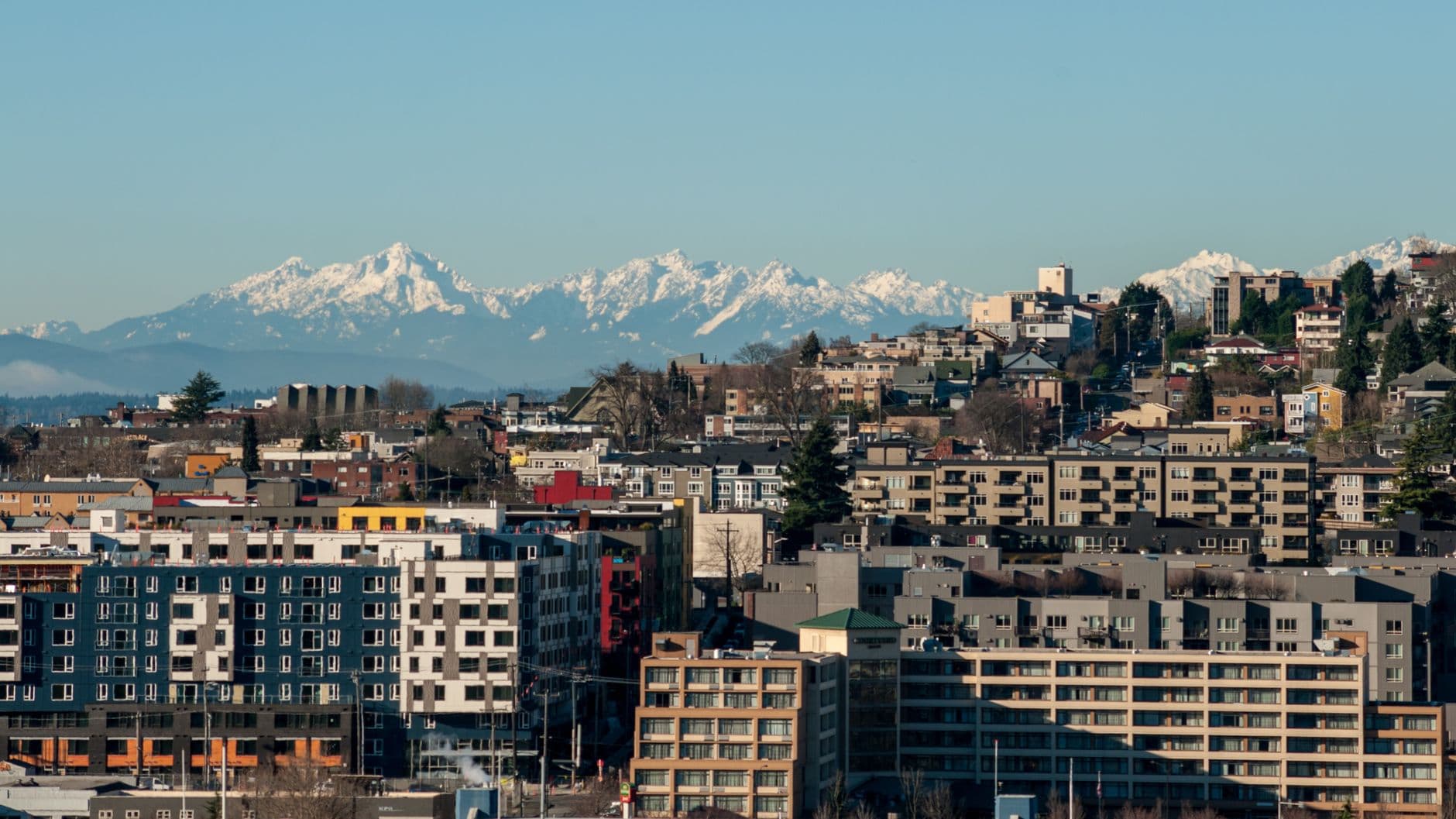A vibrant cityscape with modern buildings against a backdrop of snow-capped mountains.
